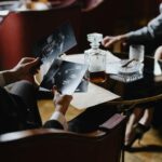 A detective analyzes black-and-white photos with a whiskey decanter and cigar on a table, creating a classic noir ambiance.