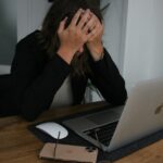 a woman covering her face while looking at a laptop