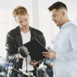 Two men reviewing documents in a motorcycle dealership, discussing a purchase agreement.