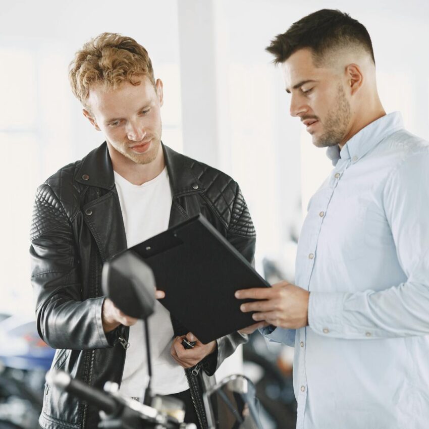 Two men reviewing documents in a motorcycle dealership, discussing a purchase agreement.