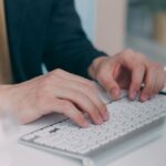 Close-up of hands typing on a white keyboard in an office setting. Ideal for business or technology themes.