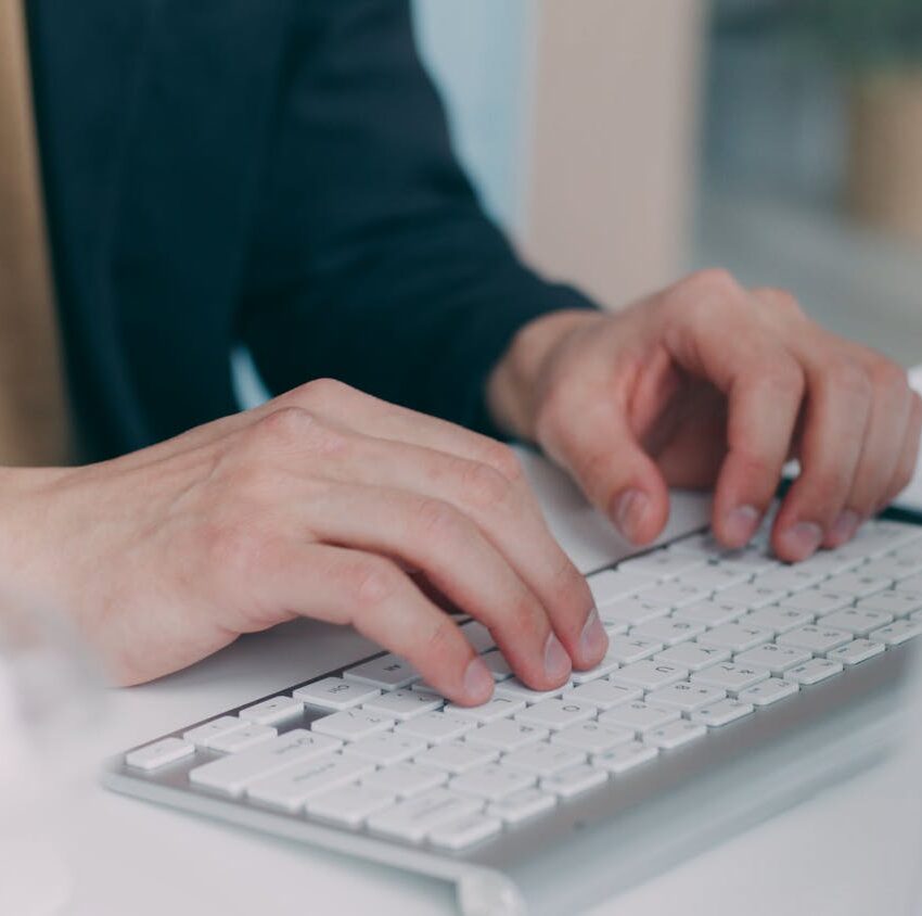 Close-up of hands typing on a white keyboard in an office setting. Ideal for business or technology themes.