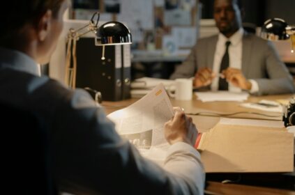 Two businessmen discuss strategies over documents in a well-lit office setting.